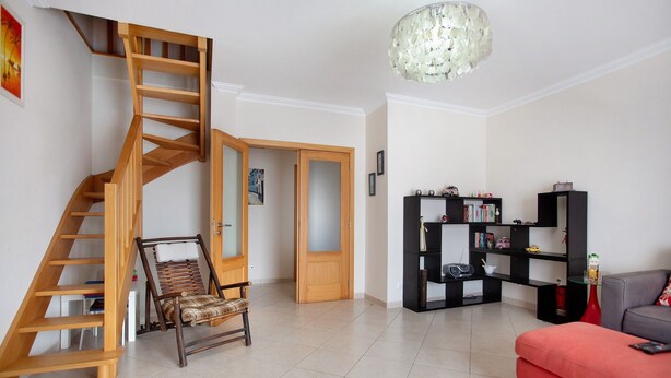Un salon avec un escalier en bois, un canapé rouge, une bibliothèque noire et un lustre.