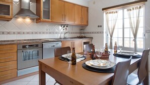 Une cuisine moderne avec des meubles en bois, des appareils en acier inoxydable et une table à manger pour deux personnes, agrémentée de verres et de bouteilles.