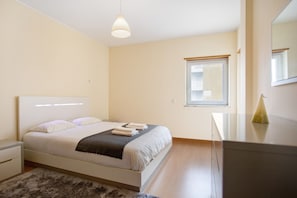 Une chambre à coucher comprenant un lit, une table de chevet, une lampe, une fenêtre et une commode.