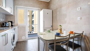 Een kleine keuken met een wasmachine, een koelkast en een eettafel met stoelen.
