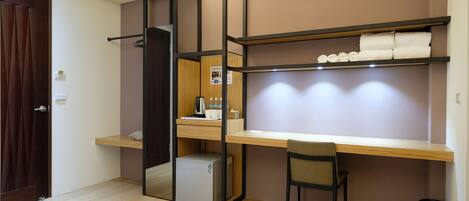 A compact room with a desk, chair, and shelves with towels.