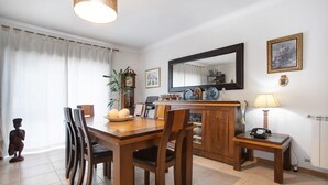 A dining area with a wooden table, chairs, a clock, a mirror, and a lamp. - Apartment 'Casa Da Mãe Maria' with Sea View, Shared Terrace and Wi-Fi (Buarcos)