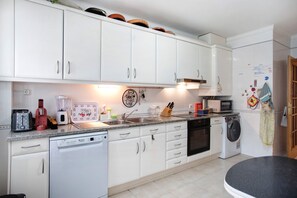 Een keuken met witte kastjes, een vaatwasser, een magnetron en een wasmachine.