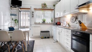 A modern kitchen with white cabinets, a dishwasher, an oven, and a dining area with a table and chairs. - Apartment 'Casa Da Mãe Maria' with Sea View, Shared Terrace and Wi-Fi (Buarcos)