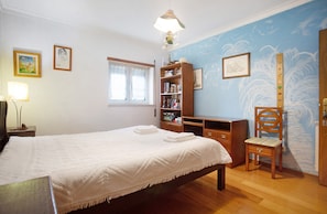 Een slaapkamer met een bed, een houten stoel, een boekenkast, een raam en wanddecoratie.