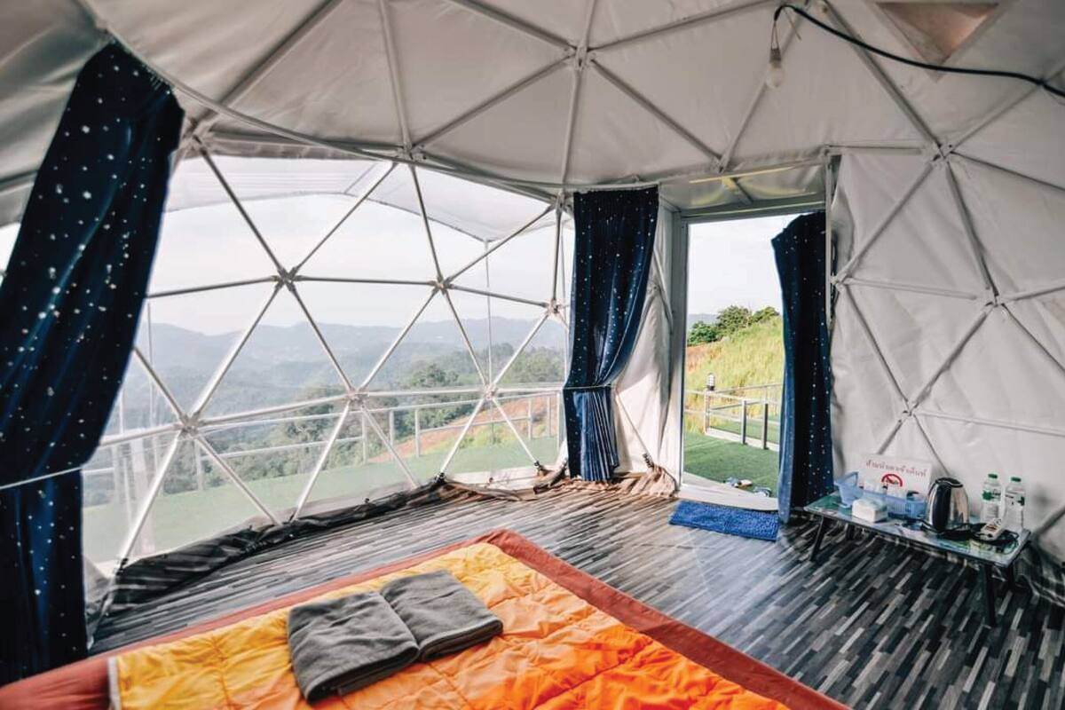 A spacious tent with a bed, a table with items, and a view of the outdoors.