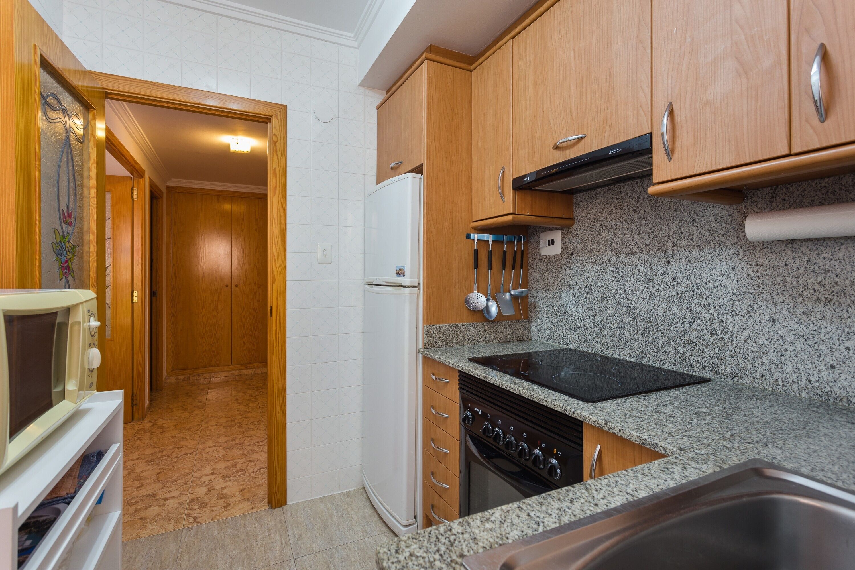 A kitchen with wooden cabinets, a white refrigerator, a stove, and a granite countertop.