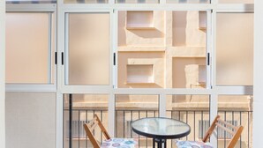 A balcony with two wooden chairs and a glass table, a white wall, and a beige building in the background. - Apartment 'Bonanza' with Private Terrace and Wi-Fi (Gandia)