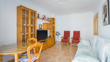 Una sala de estar con una mesa de comedor, sillas, un sofá, un televisor, armarios de madera y un ventilador.