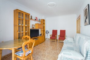 Un salon comprenant une table à manger, des chaises, un canapé, un téléviseur, des meubles en bois et un ventilateur.