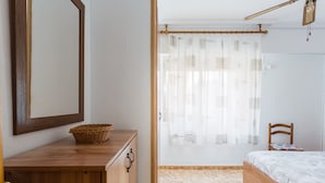 A bedroom with a wooden dresser, a bed, a wicker basket, and a window with sheer curtains. - Apartment 'Bonanza' with Private Terrace and Wi-Fi (Gandia)