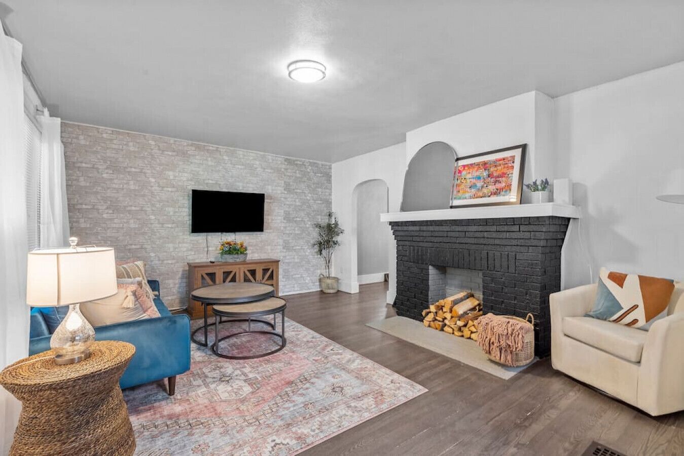 A living room with a fireplace, a TV mounted on the wall, a blue sofa, a beige armchair, and a round coffee table.