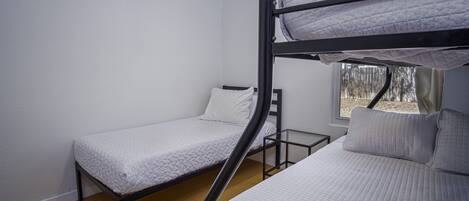 A dormitory room with bunk beds, a window with a view of trees, and a wooden floor.