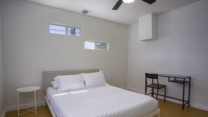 Un dormitorio con una cama, un escritorio y dos ventanas pequeñas.