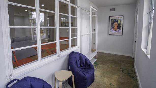 Una habitación con un ventanal grande, un sillón de saco, un taburete pequeño y un cartel en la pared.