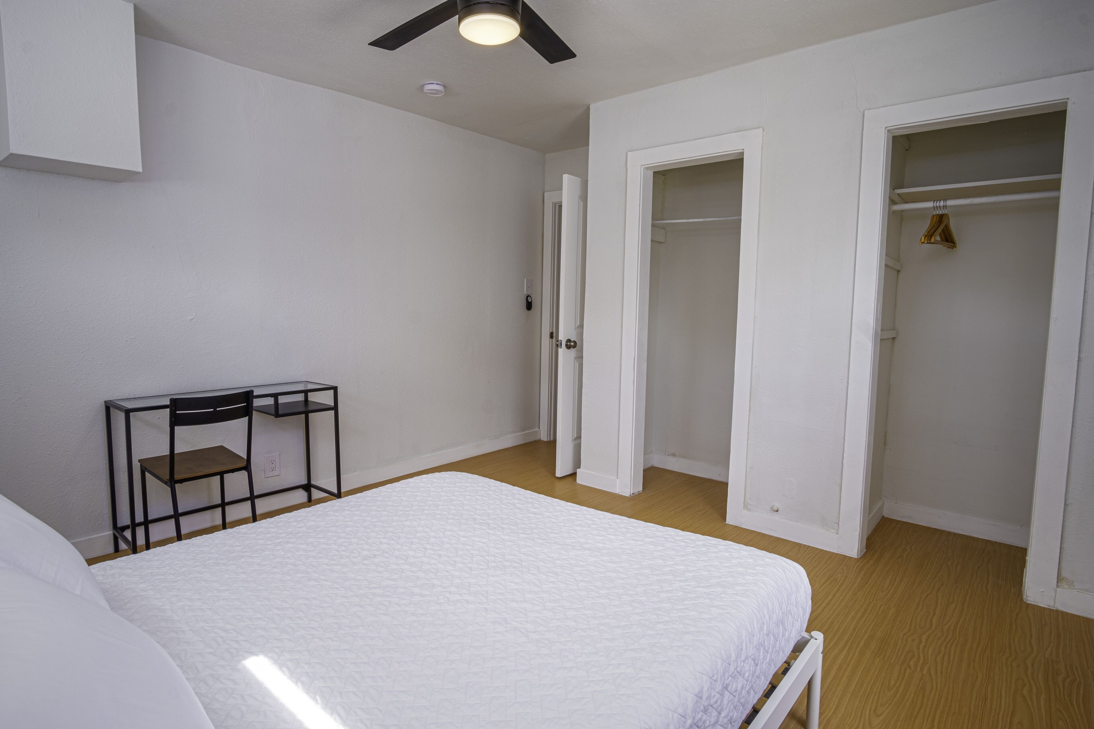 A bedroom with a bed, a desk with a chair, and two open closets.