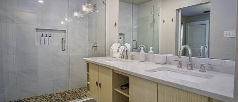 A modern bathroom with a glass-enclosed shower, a large mirror, and a double sink vanity.