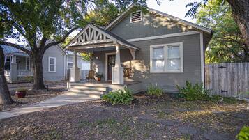 A two-story house with a porch, a front yard with a tree, and a wooden fence.