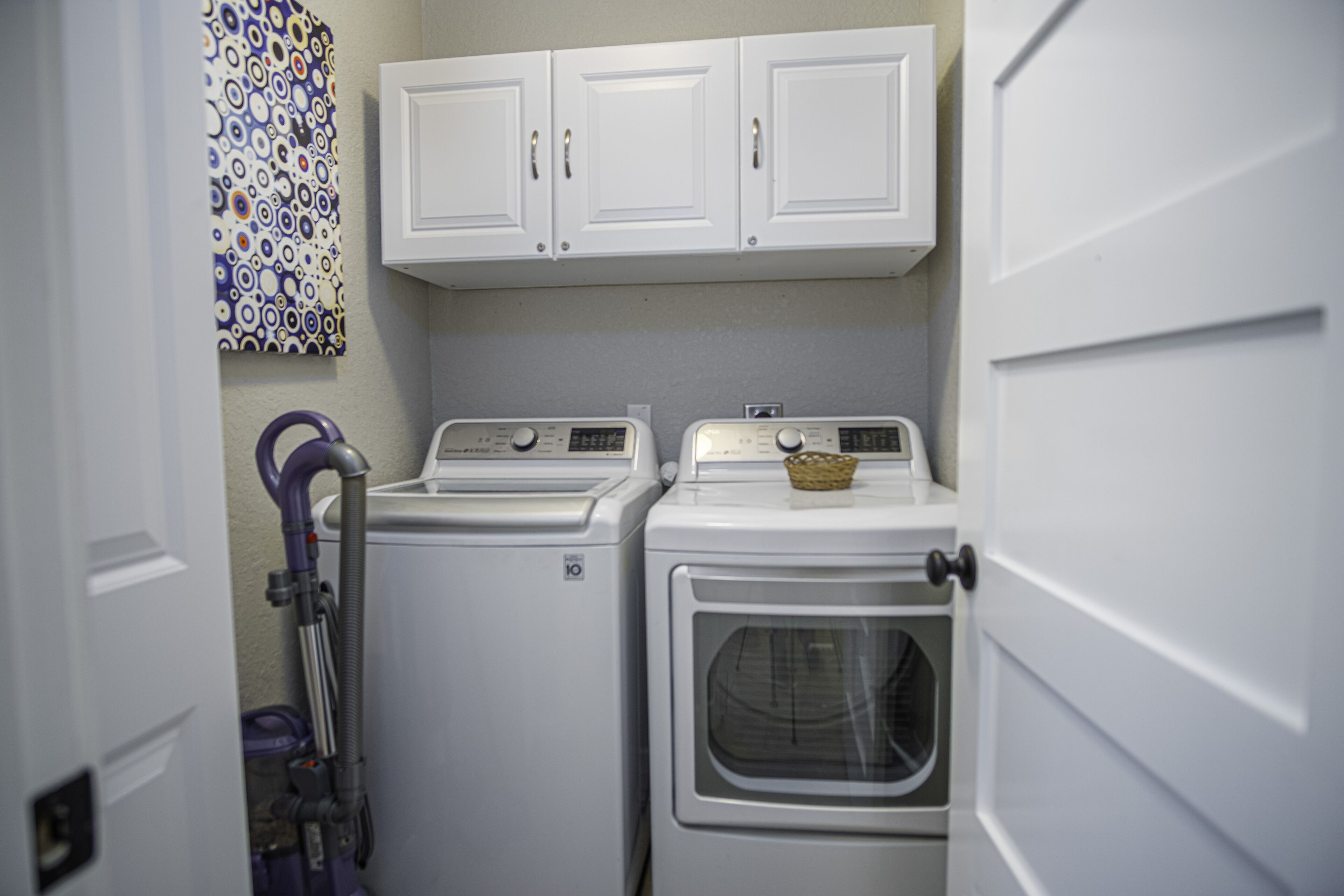 A laundry room with two stacked washers and dryers, a basket on the dryer, and a vacuum cleaner.
