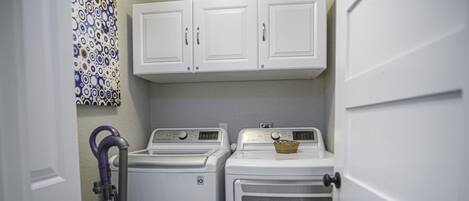A laundry room with two stacked washers and dryers, a basket on the dryer, and a vacuum cleaner.