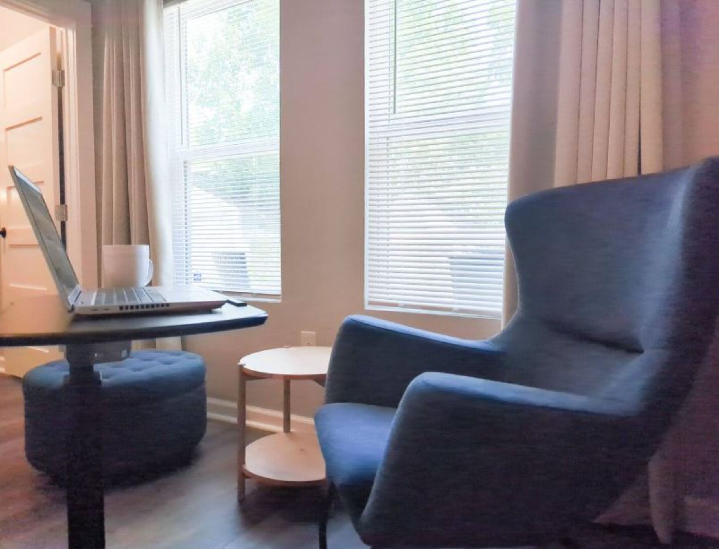 A room with a blue armchair, a laptop on a small table, and a white cup.
