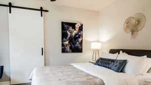 A modern bedroom with a large bed, a wall-mounted fan, and a painting. - Charming Studio W/deck & Garden (San Antonio)