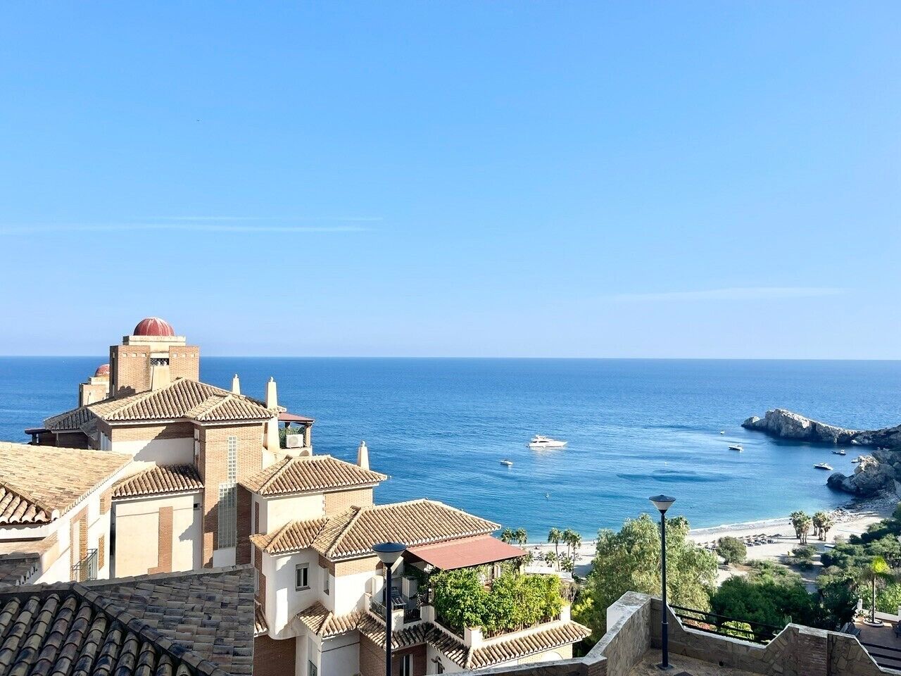 A coastal town with Mediterranean architecture, a clear view of the sea, and rocky outcrops.