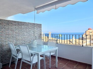 Un balcón con una mesa y sillas, un muro de ladrillo y vista al mar.