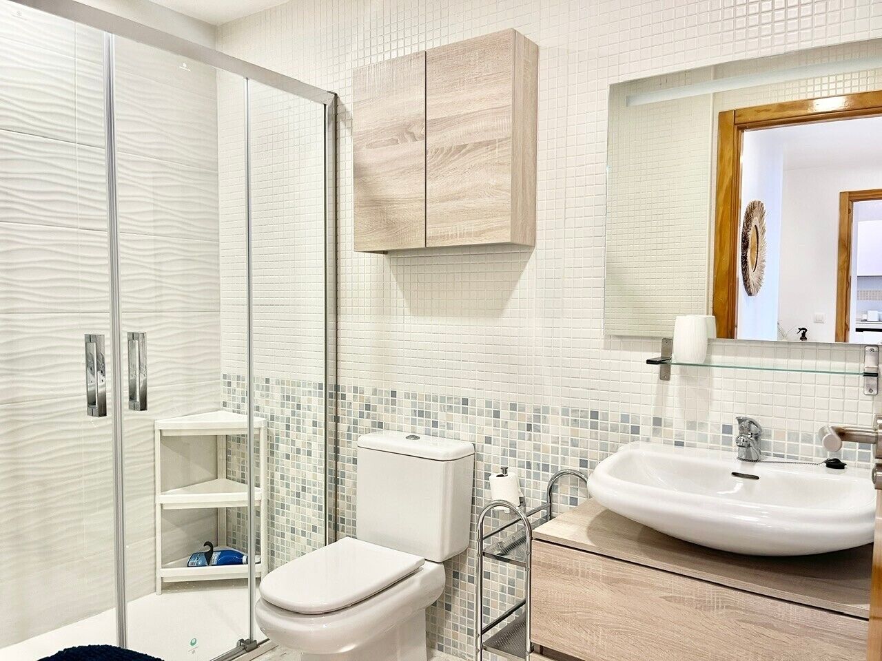 Une salle de bain moderne avec une douche à parois de verre, des toilettes blanches, un lavabo avec un miroir au-dessus et un meuble en bois.