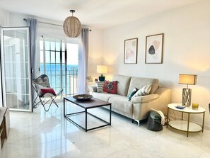 Un salón con sofá, mesa de centro y sillón. Cuenta con un balcón y vistas.