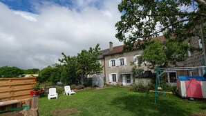 Un jardin avec un banc en bois, des chaises blanches, une balançoire et un petit abri de jardin.