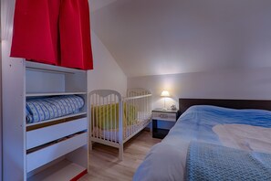 Une chambre avec un berceau, un lit, une table de chevet et une armoire.