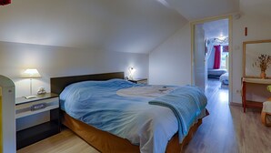Une chambre à coucher avec un lit, une table de chevet, une lampe et une vue sur une autre pièce.