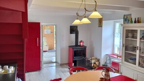 Une cuisine avec un poêle rouge, une table à manger avec des chaises et un buffet rempli de vaisselle.