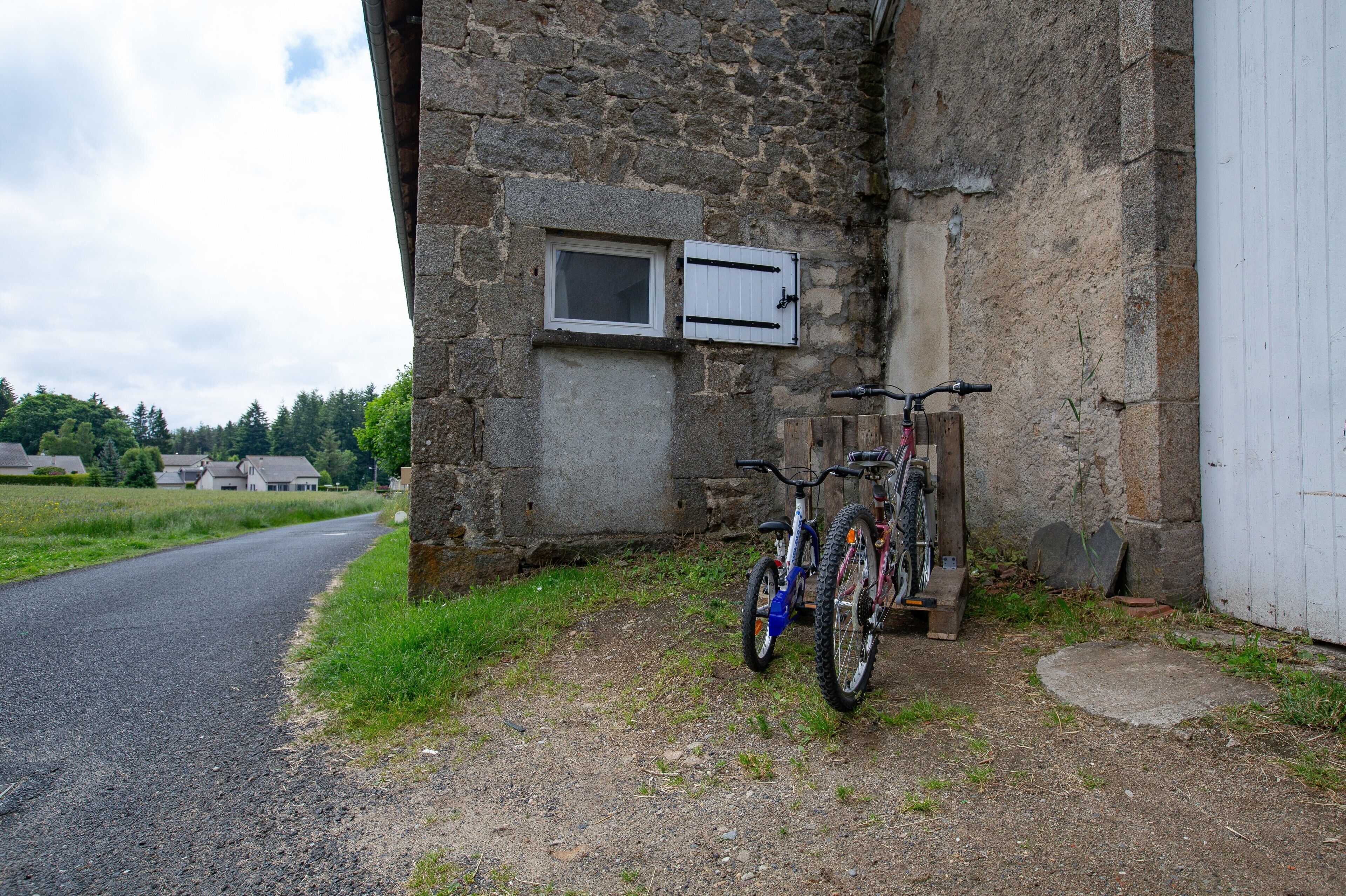 En bygning i sten med et vindue, en dør, en cykel og en asfalteret vej.