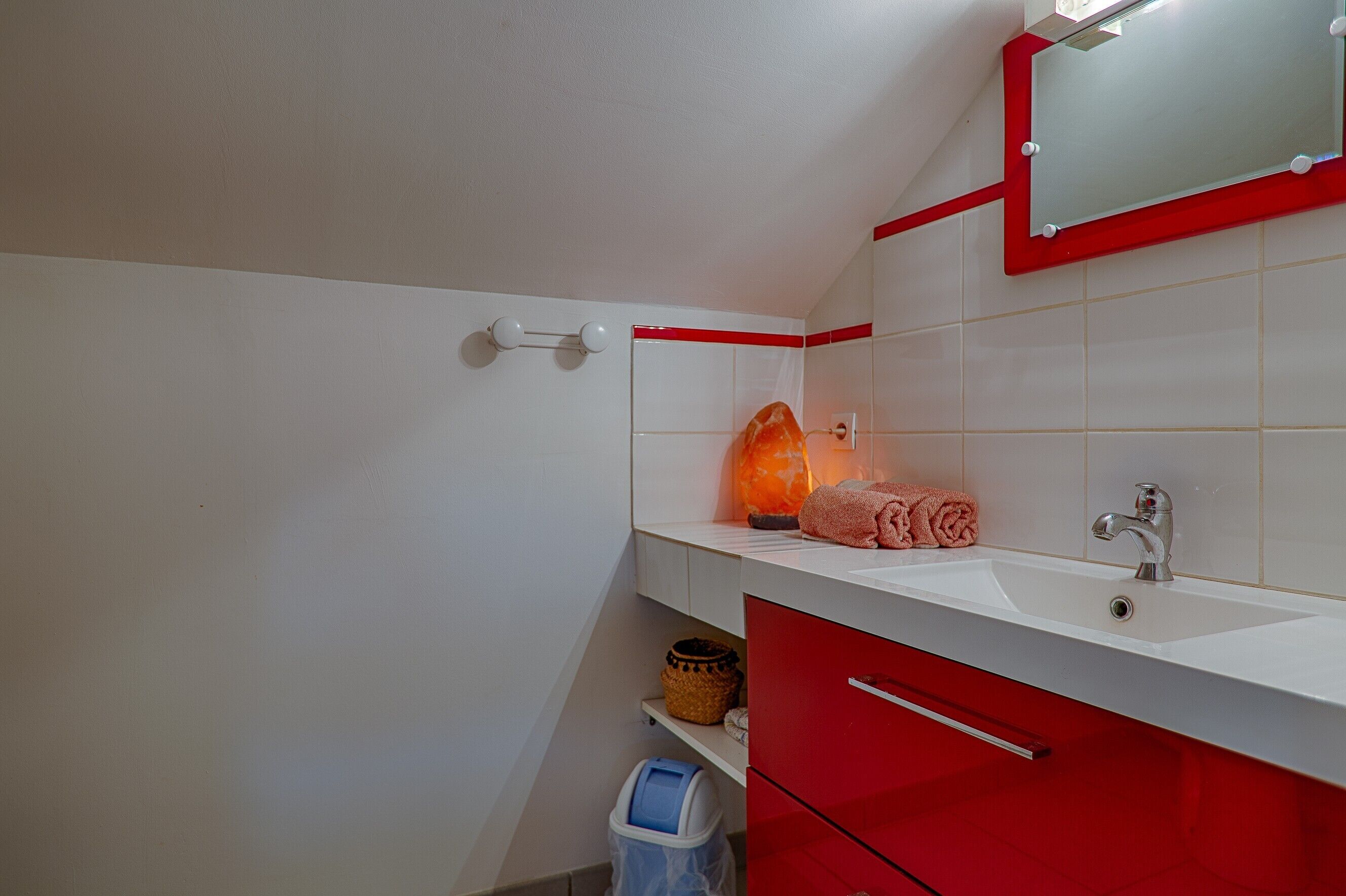 Een badkamer met een witte wastafel, een rode kast en een spiegel met een rode lijst.