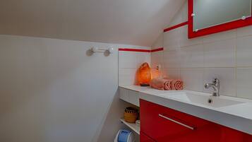 Een badkamer met een witte wastafel, een rode kast en een spiegel met een rode lijst.