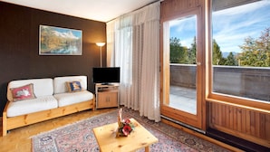 A living room with a sofa, TV, table with flowers, and a large window.