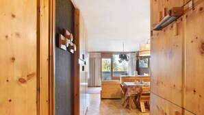 A wooden interior with a dining area, a kitchen, and a view through a window.