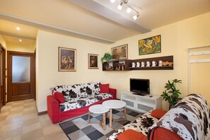 A living room with a sofa, two small tables, a TV, and shelves with decorative items. - Augusta Praetoria – Spacious Apartment in the Heart of Aosta, Near Pila and the Alps (Aosta)