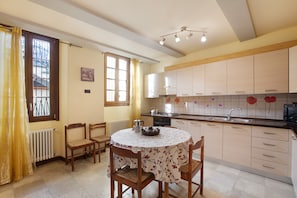 A kitchen with a round table, chairs, a radiator, a window with curtains, and cabinets. - Augusta Praetoria – Spacious Apartment in the Heart of Aosta, Near Pila and the Alps (Aosta)