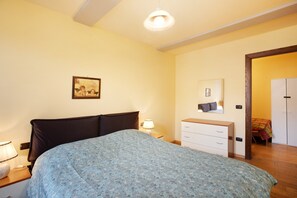 A bedroom with a bed, bedside table, lamp, dresser, mirror, and wardrobe. - Augusta Praetoria – Spacious Apartment in the Heart of Aosta, Near Pila and the Alps (Aosta)