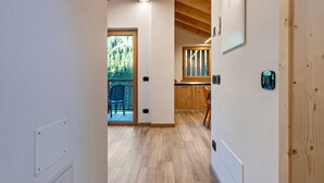 Un pasillo con piso de madera, una puerta que da a un balcón y una zona de cocina con armarios de madera.