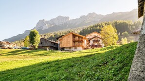 Un pueblo de montaña con casas de madera, una colina cubierta de hierba y montañas al fondo.