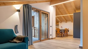 Un interior moderno con un sofá color turquesa, suelo de madera, una zona de comedor con sillas y una mesa, y un ventanal corredero que da a otra habitación.