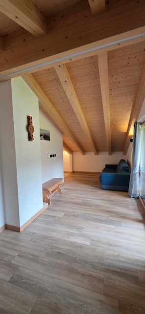 An attic room with wooden beams, a bench, a blue sofa, and a wooden wall clock.