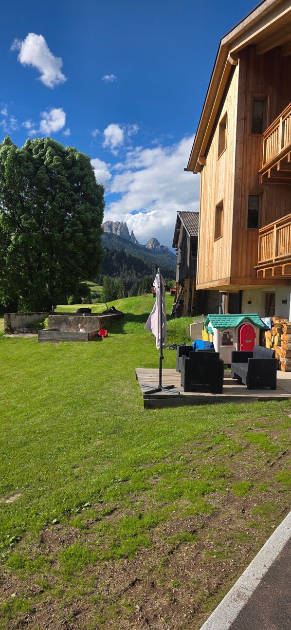 Un edificio de madera con balcón, zona ajardinada y vista a la montaña.