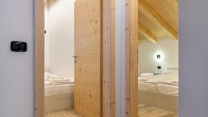 Una habitación con puerta de madera, una cama con ropa de cama blanca y una mesita de noche con lámpara.