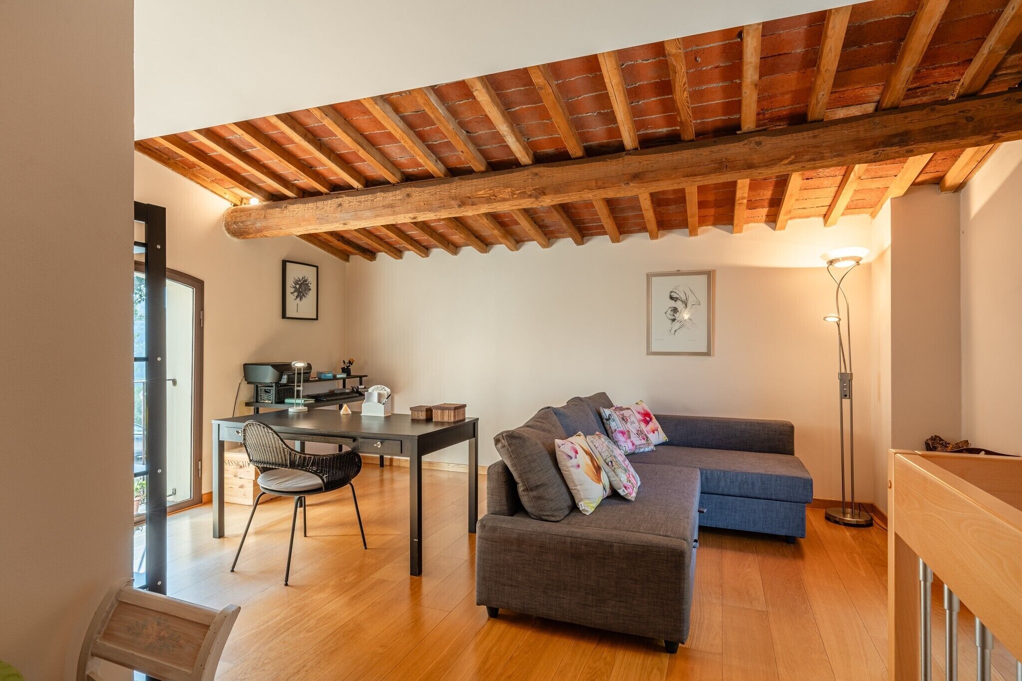 Ein Wohnzimmer mit Holzbalkendecke, einer Couch, einem Esstisch und einer Stehlampe.