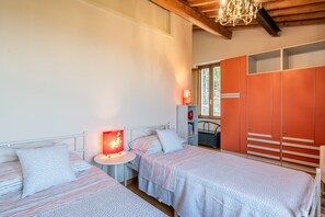 A bedroom with two beds, a nightstand, a red lamp, a wardrobe, and a window.